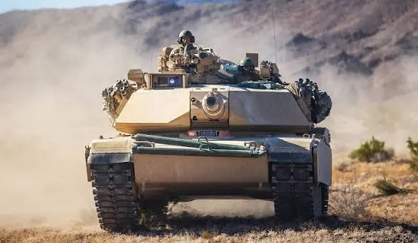 M1 Abrams tank and crew moving through dust during maneuvers