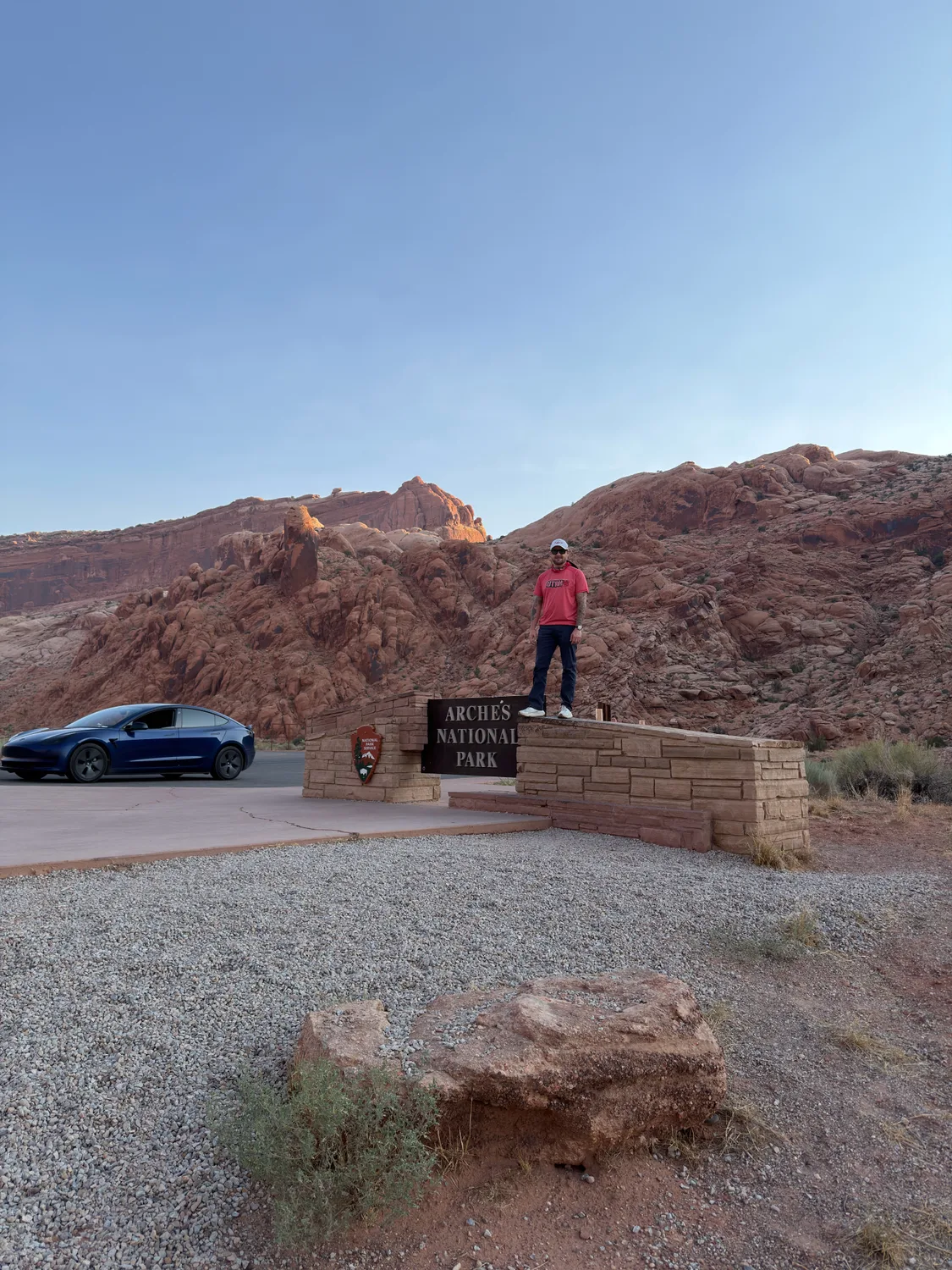 Brison McPhail standing on the Arches National Park entrance sign