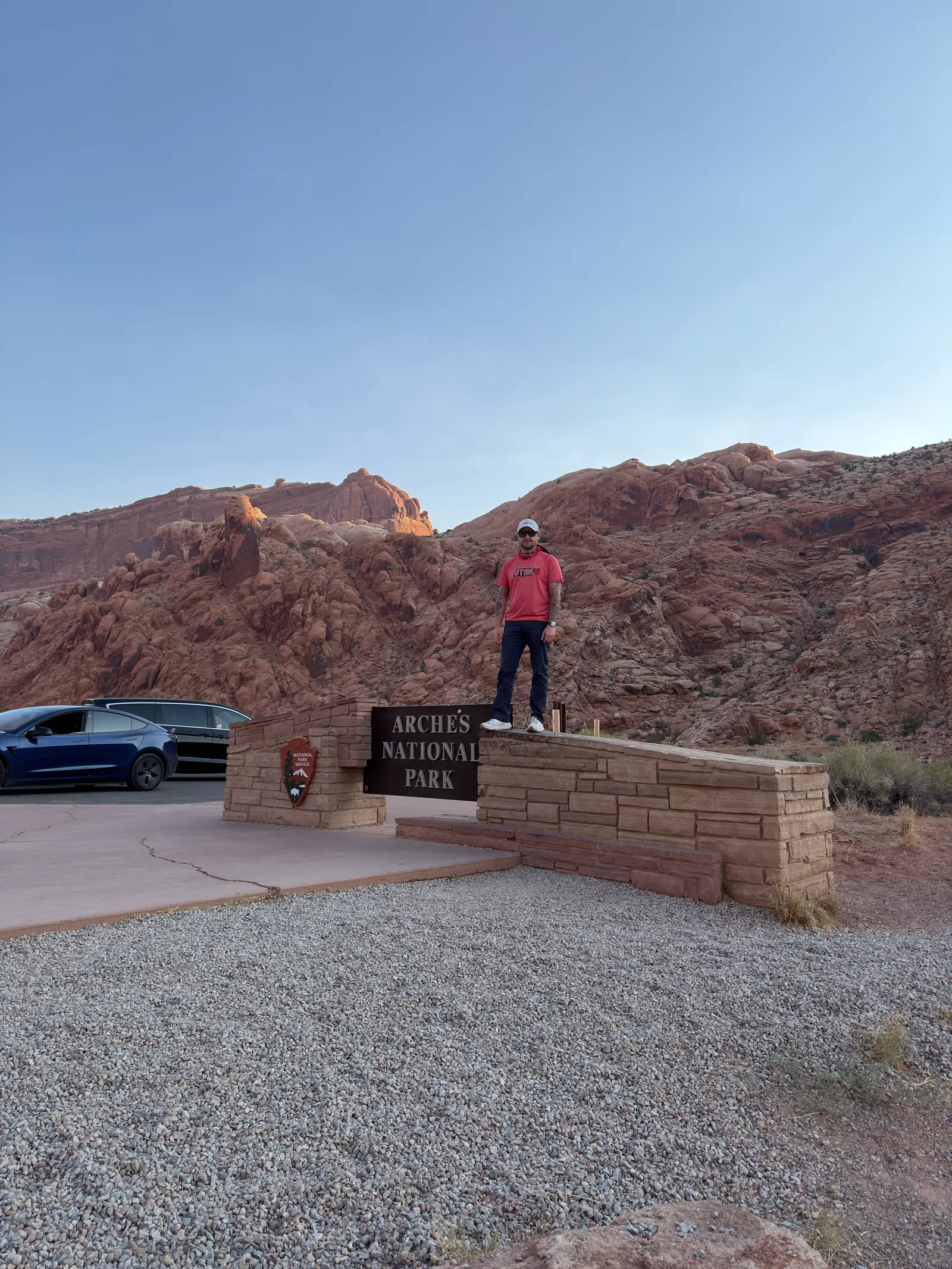 Standing on top of the Arches National Park entrance sign at dawn, red rock behind