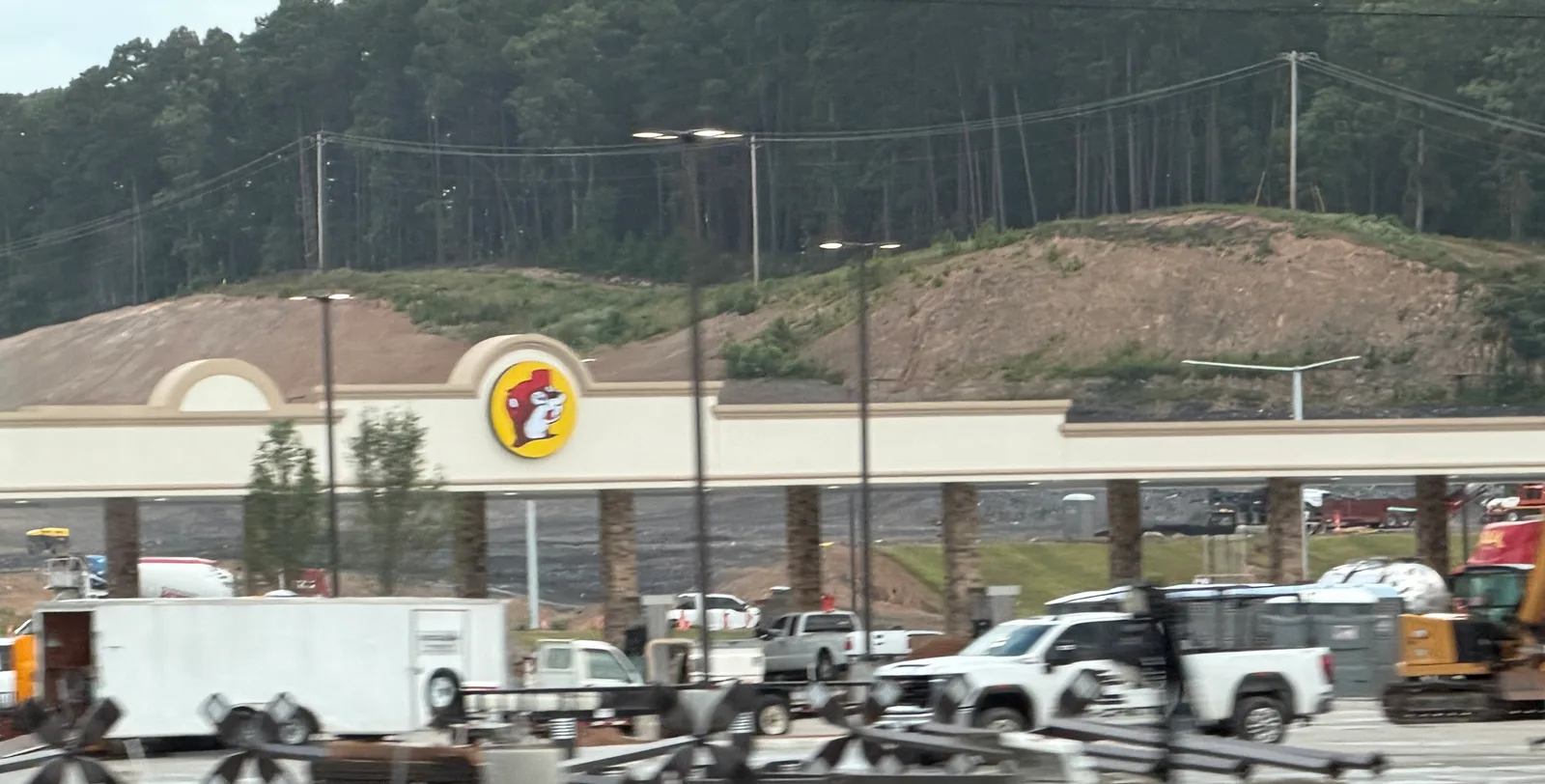 The Benton, Arkansas Buc-ee's under construction off I-30 — storefront, beaver logo, and fuel canopy taking shape against the cut hillside