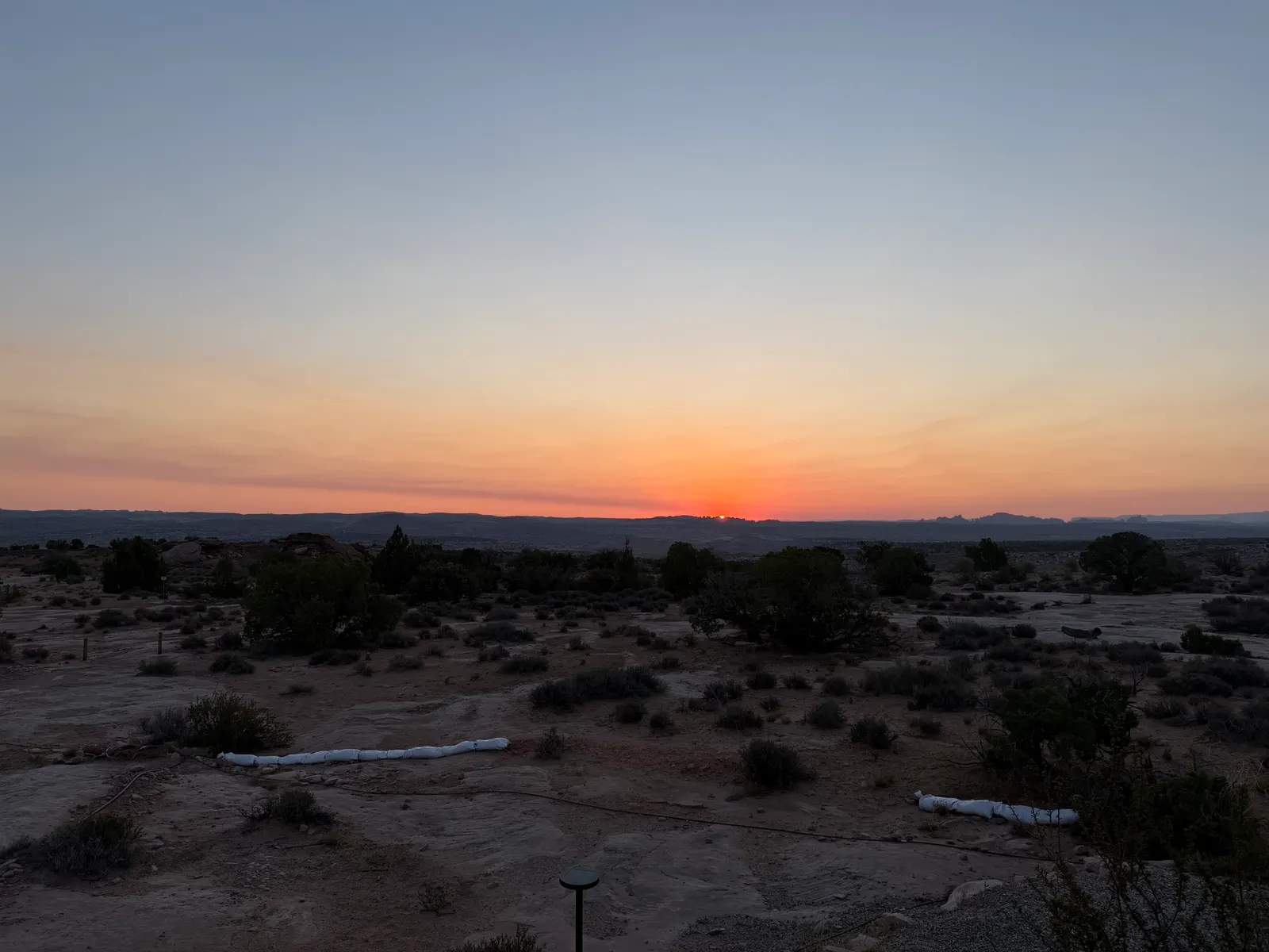 Sunrise breaking over the desert horizon at Under Canvas Moab, junipers and tent platforms in the dawn light