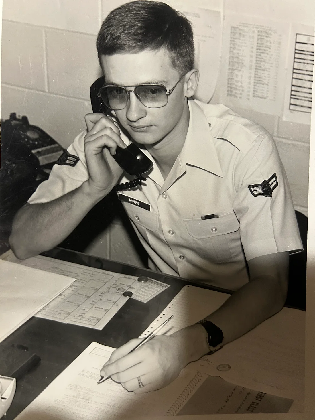 Brison McPhail's father as an Airman First Class in U.S. Air Force khakis, name tape McPhail, on the phone at a duty desk