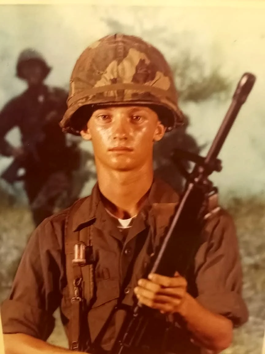Brison McPhail's father as a young soldier in U.S. Army fatigues, steel helmet with camouflage cover, holding an M16 rifle in a basic training studio portrait