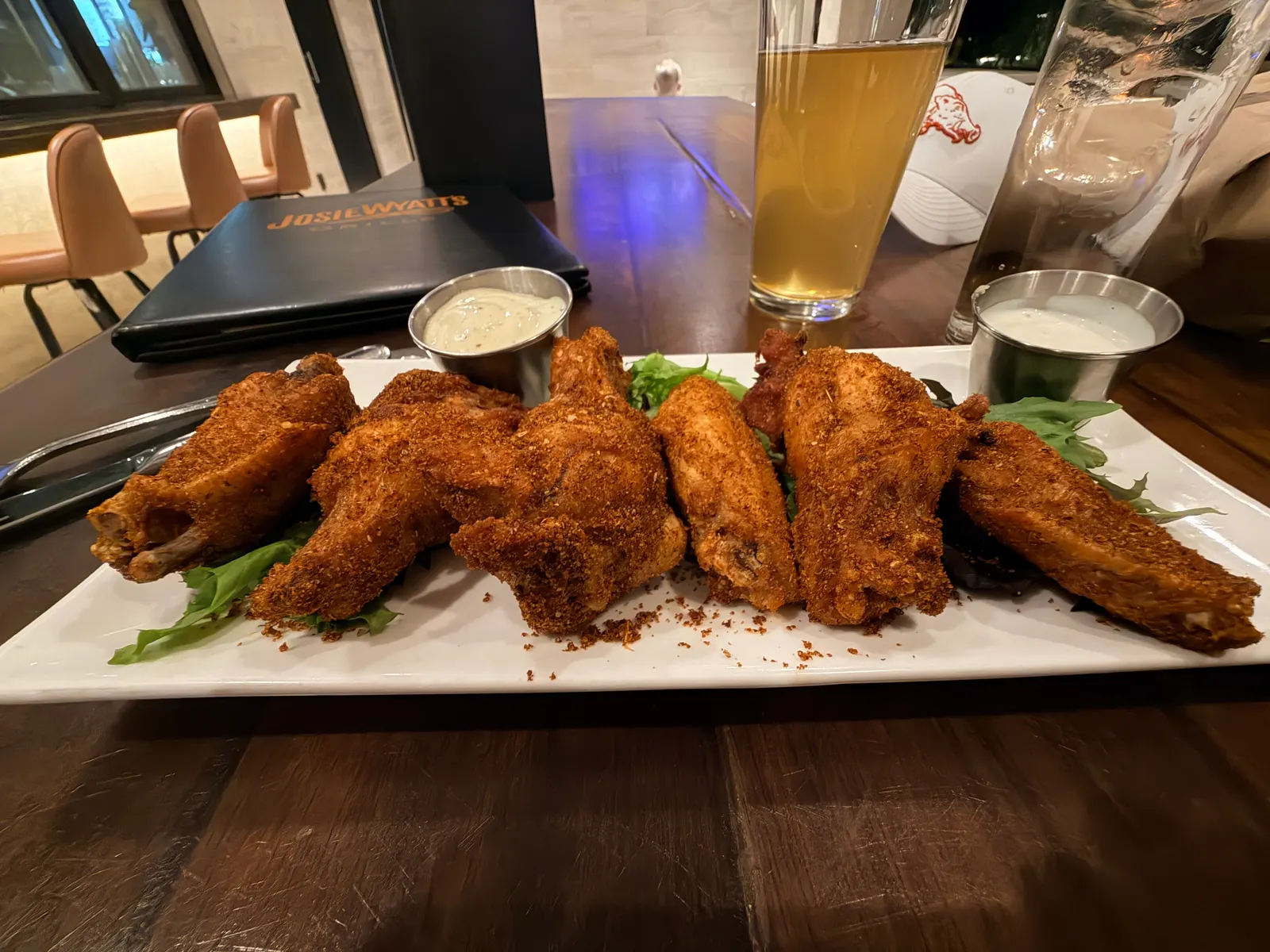 Platter of dry-rub wings with two dipping sauces at Josie Wyatt's Grille, an Arkansas Razorbacks hat on the table