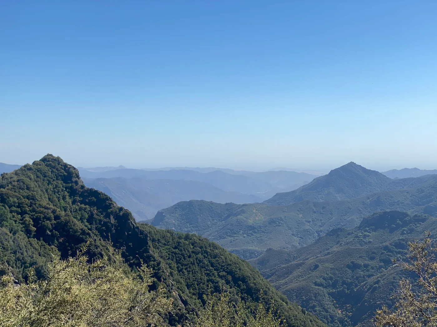 Layered mountain ridges fading into haze, seen while climbing higher into the California mountains where the air turns cooler