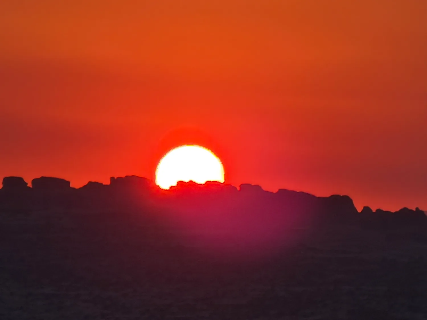 Deep red sun setting through wildfire smoke over silhouetted rock formations near Moab